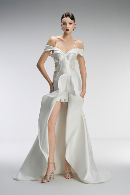 Model wearing a white off-shoulder evening gown with a high slit on a gray background