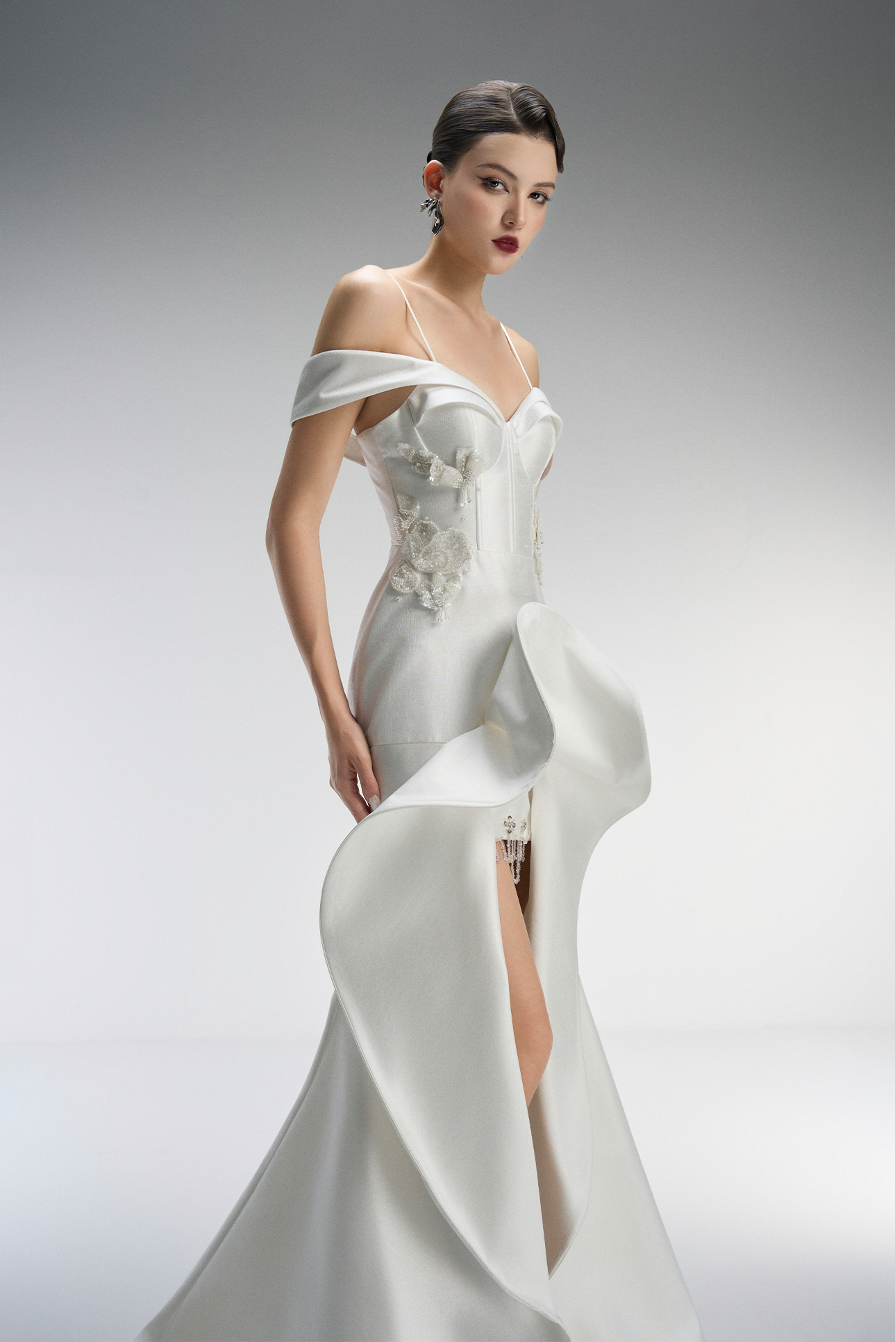 Woman wearing a white off-shoulder gown with a high slit on a gray background