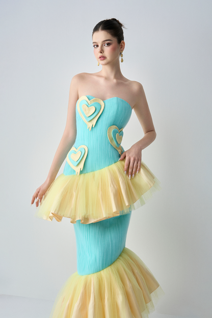 Woman wearing a strapless dress with heart designs in turquoise and yellow on a white background