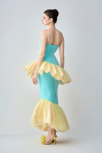 Woman wearing a strapless dress with a turquoise bodice and yellow ruffled skirt on a white background