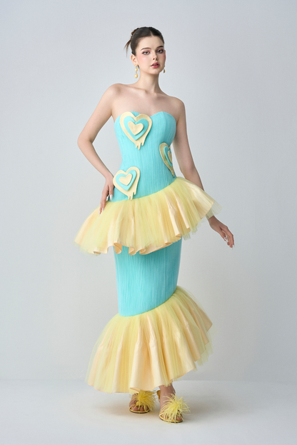 Woman wearing a strapless dress with blue top and yellow ruffled skirt on a white background