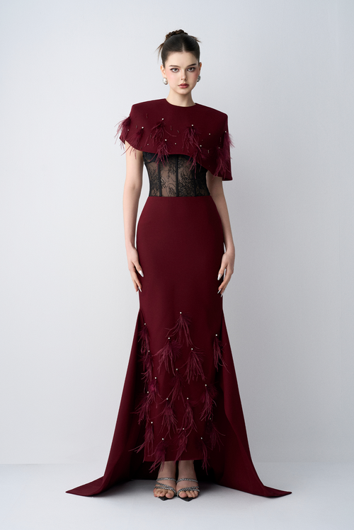 Woman wearing a burgundy evening gown with feather details on a white background