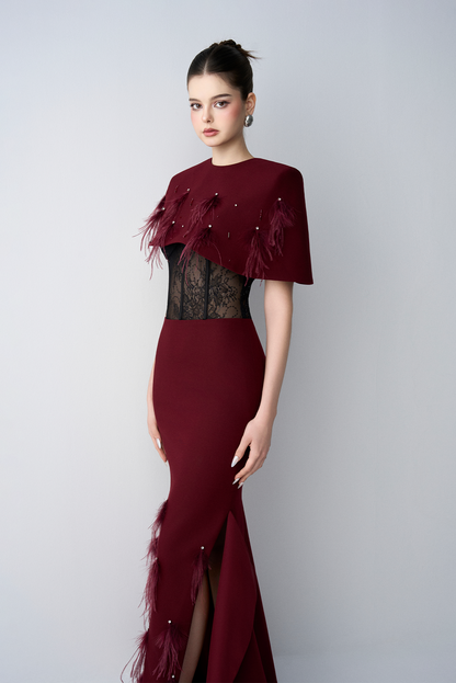 Woman wearing a burgundy evening gown with feathered details on a white background