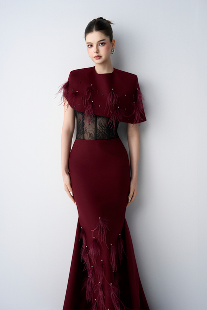 Woman wearing a burgundy evening gown with fringe details against a white background