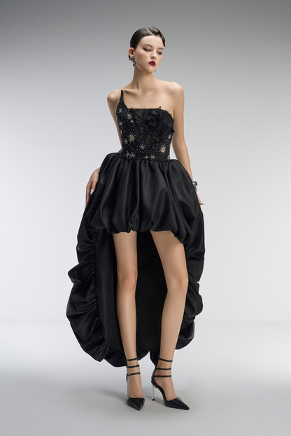 Woman wearing a black evening gown with a high-low design on a gray background