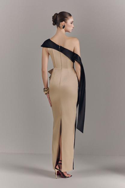 Woman wearing a beige one-shoulder dress with a black accent on a plain background