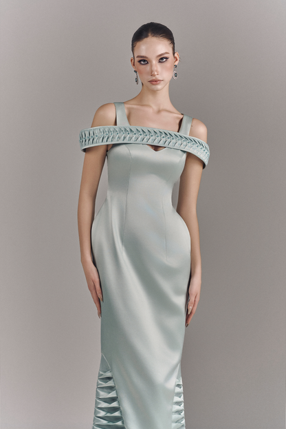 Woman wearing a light green evening gown with decorative straps against a gray background