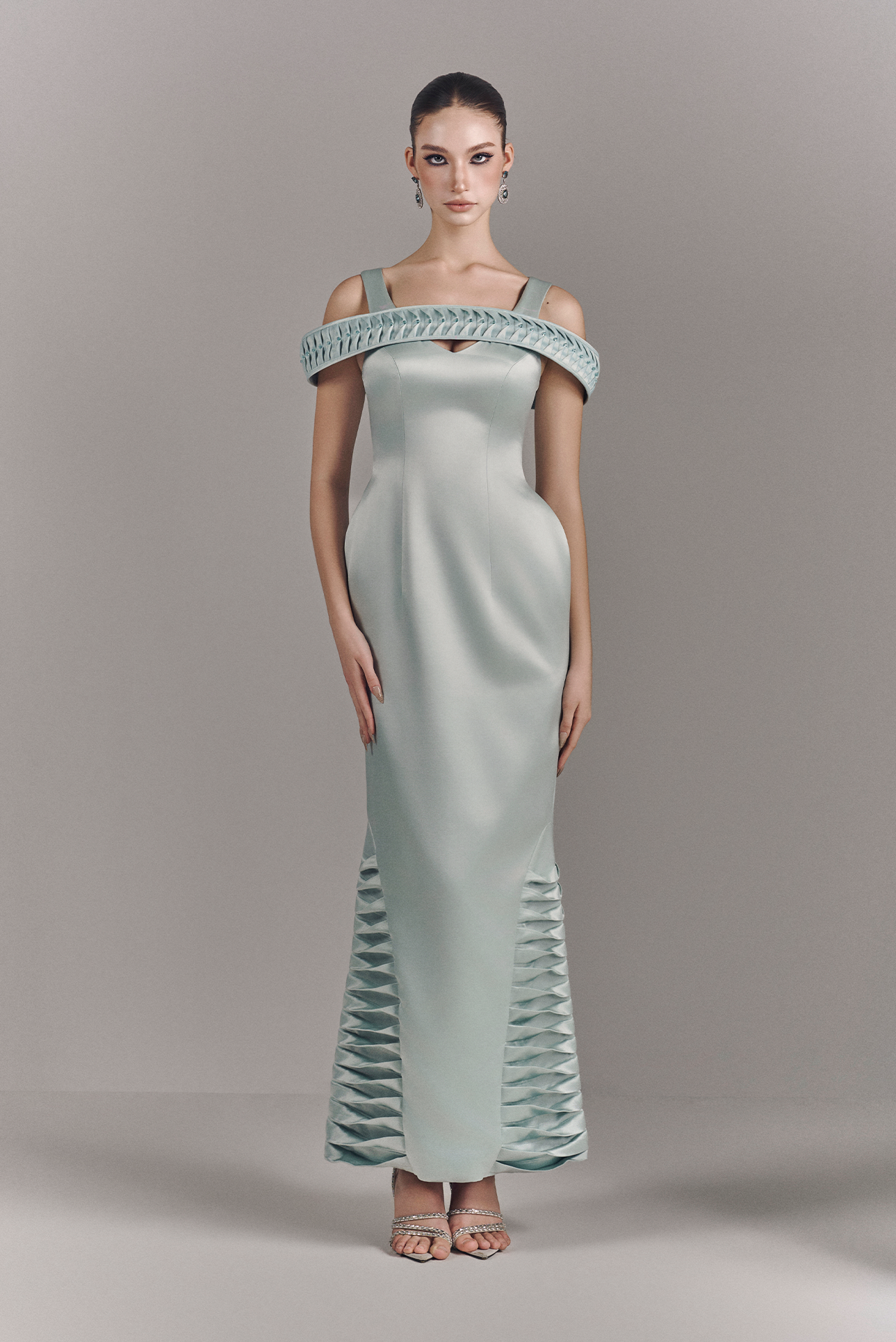 Woman wearing a light green off-shoulder evening gown with intricate detailing on a gray background