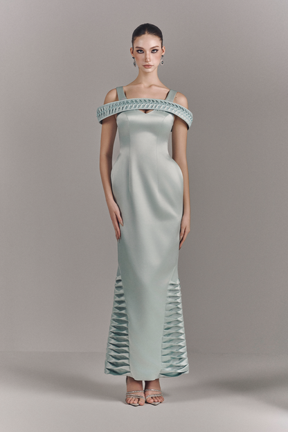 Woman wearing a light green off-shoulder evening gown with intricate detailing on a gray background
