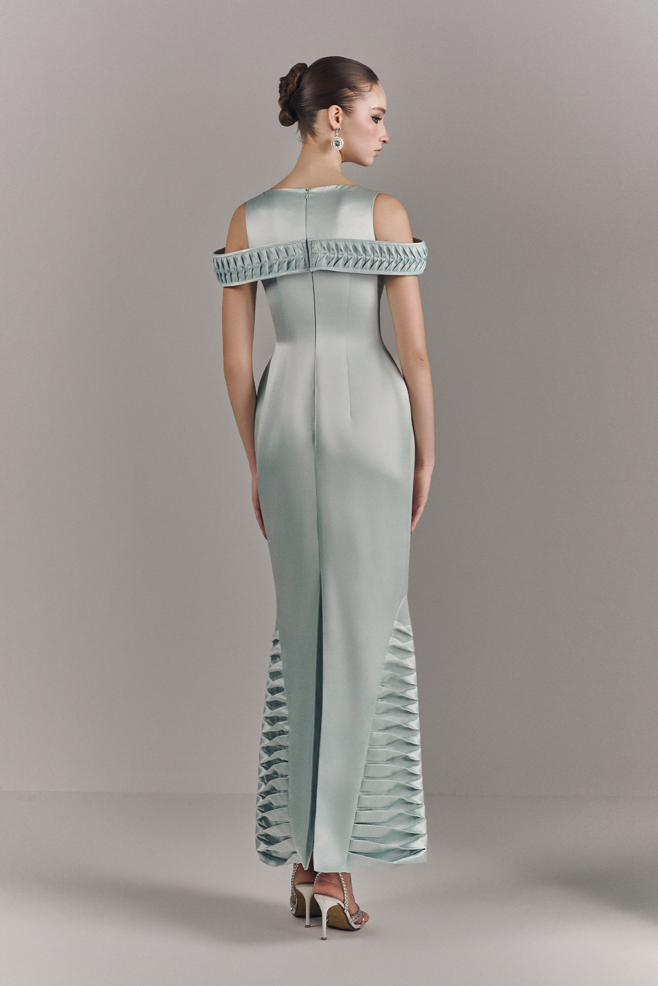 Woman wearing a light blue off-shoulder jumpsuit with ruffled details on a gray background