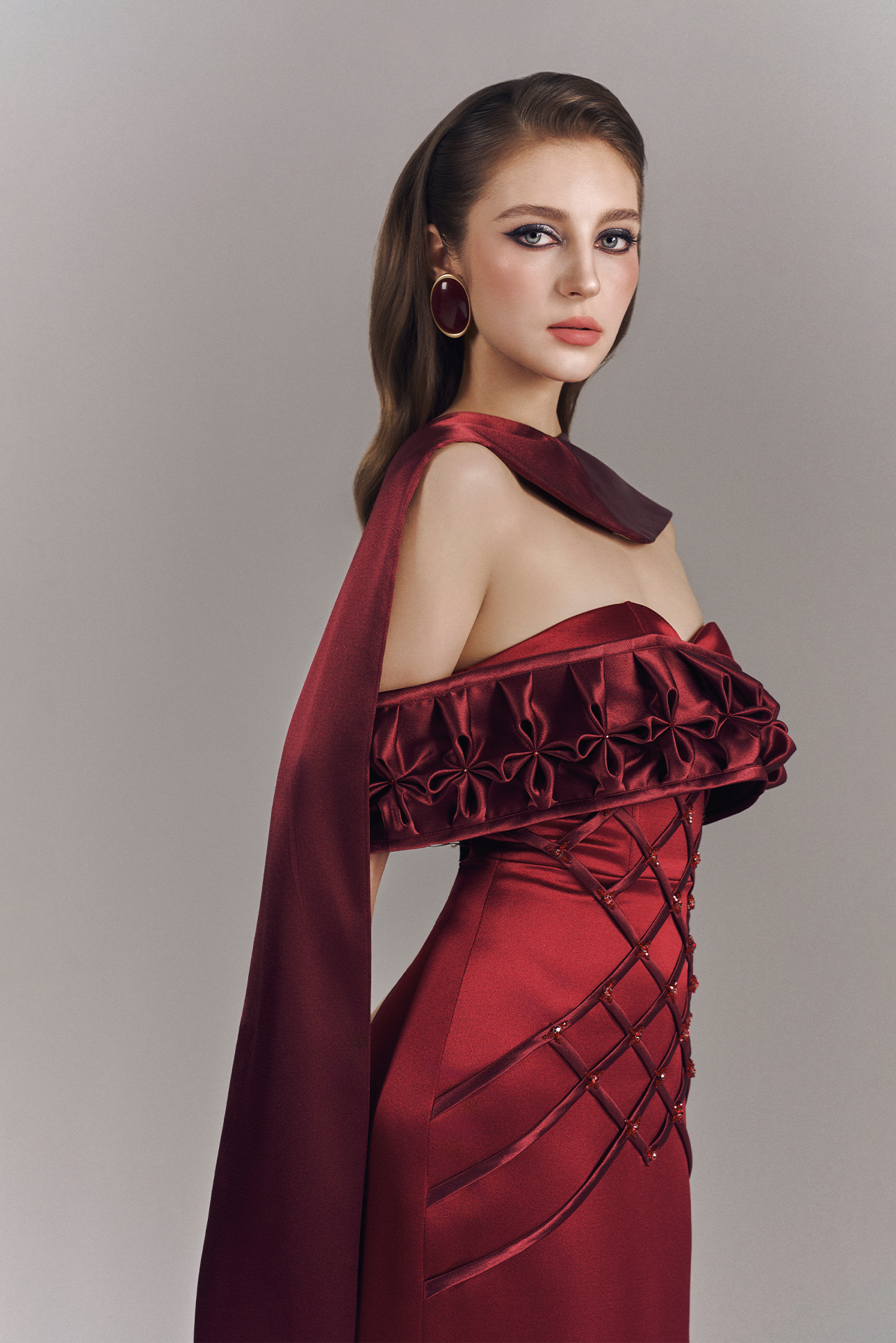Woman wearing a burgundy off-shoulder dress with a cape on a plain background
