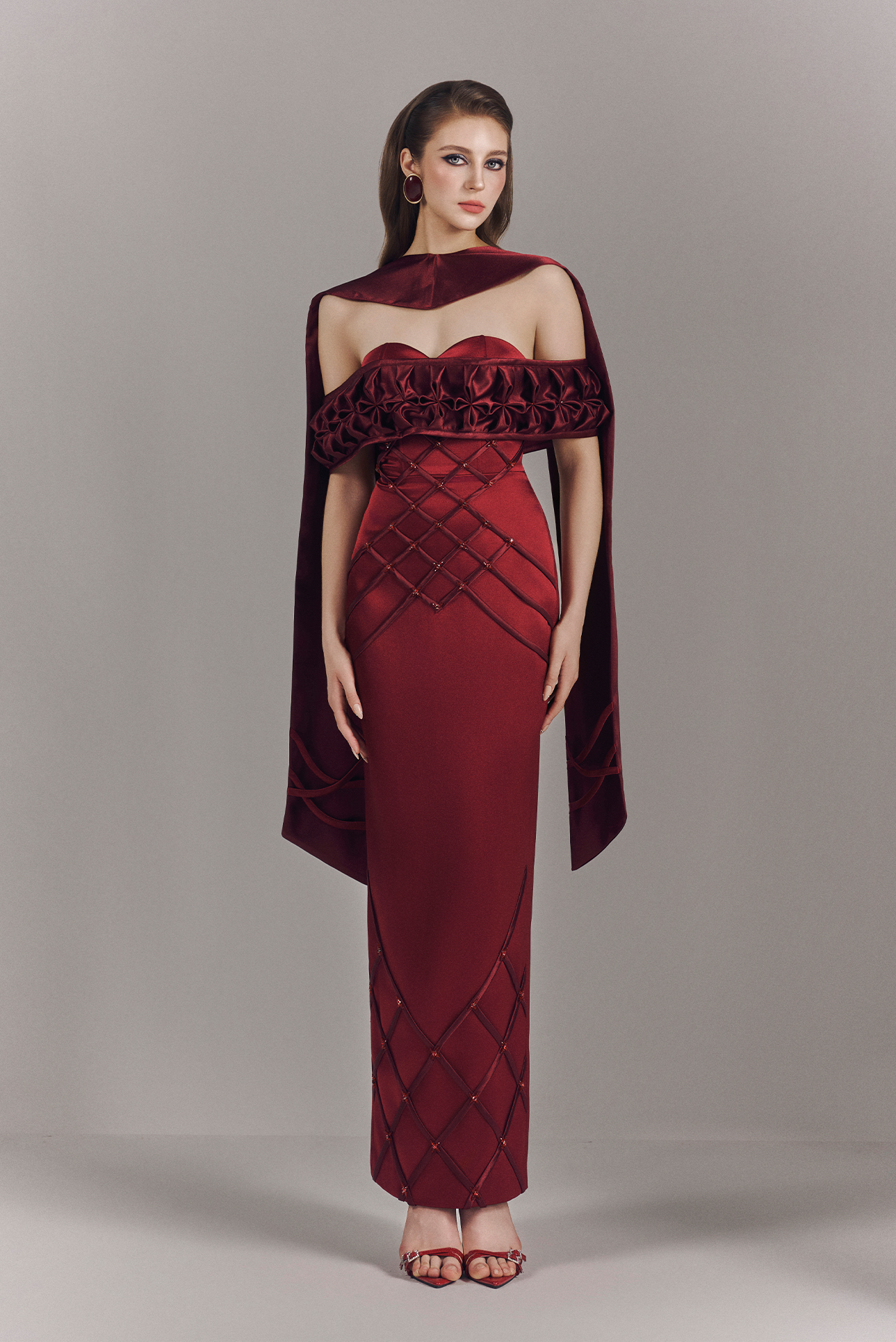 Woman wearing a burgundy evening gown with a matching cape on a gray background