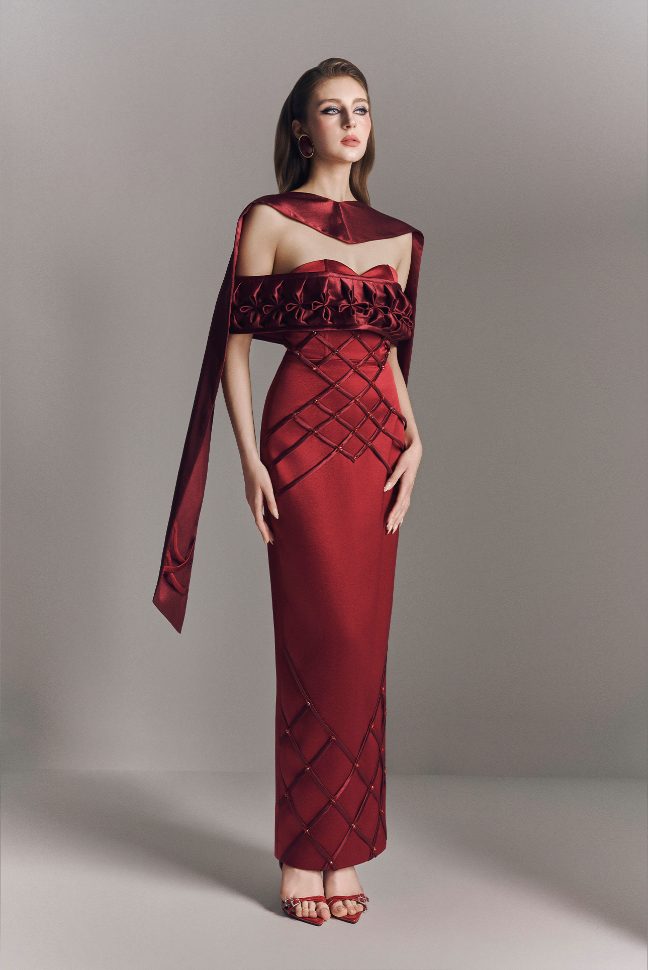 Woman wearing a red evening gown with geometric patterns on a gray background