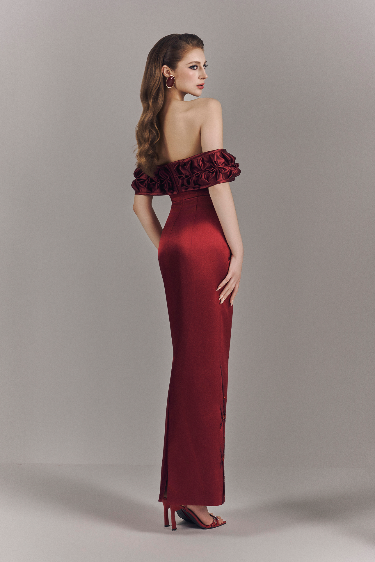 Woman wearing a red off-shoulder evening gown with floral details on a plain background