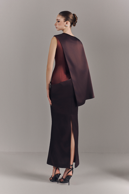 Woman wearing a burgundy evening gown with a cape on a plain background