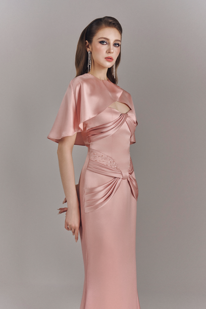 Woman wearing a pink satin evening gown with a cut-out design on a gray background