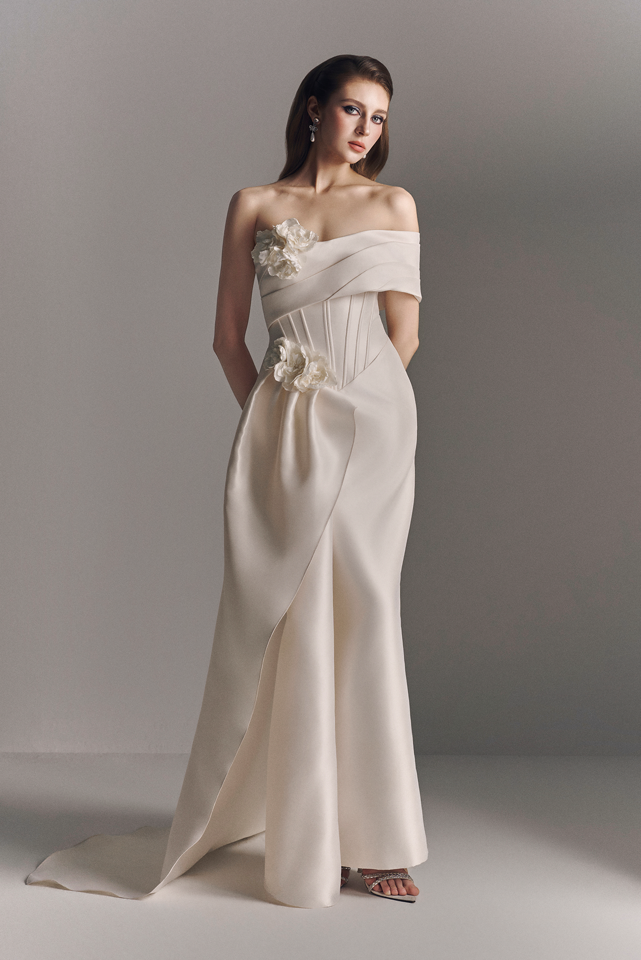 Woman wearing a white off-shoulder gown with floral details against a gray background