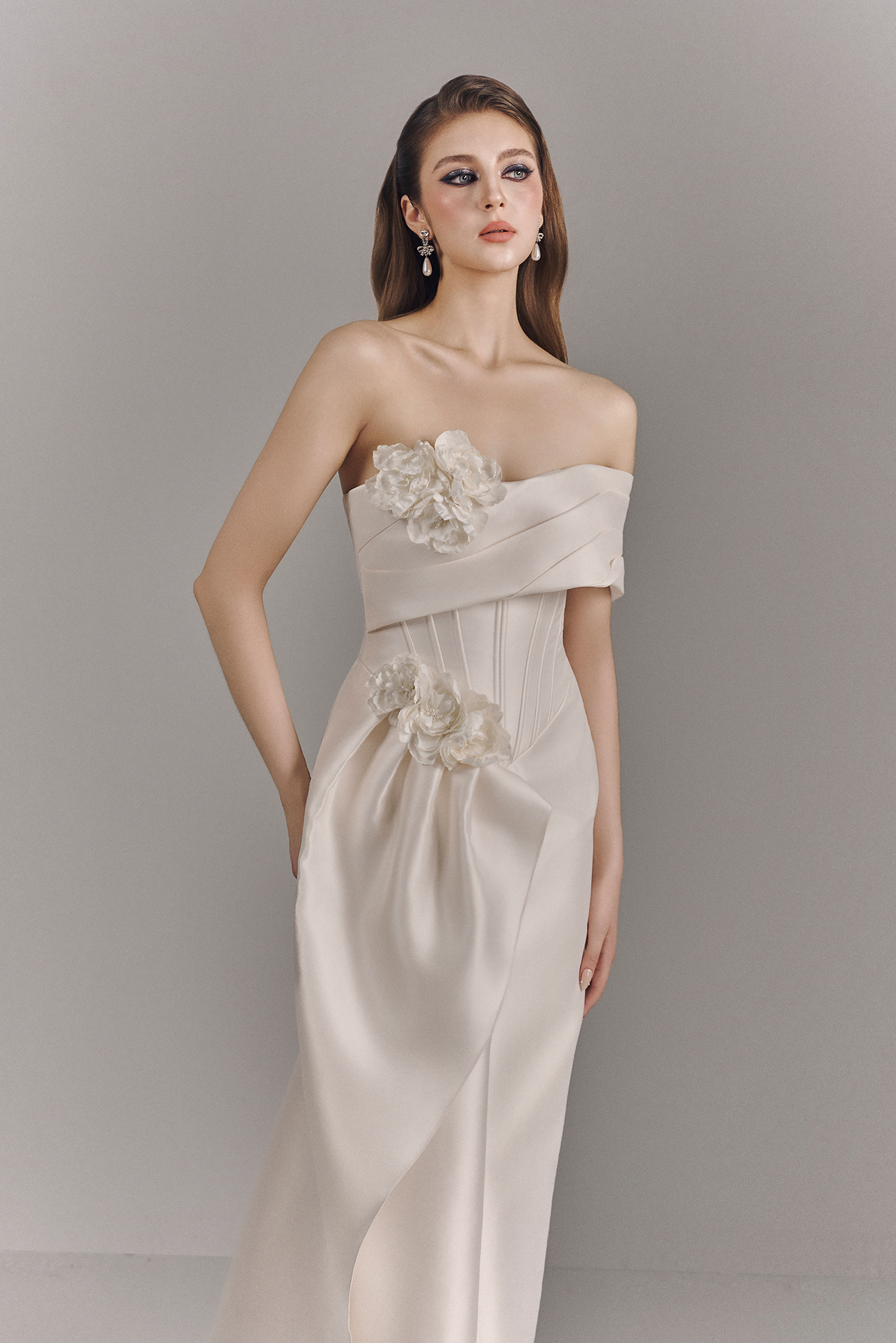 Woman wearing a strapless wedding dress with floral details on a plain background