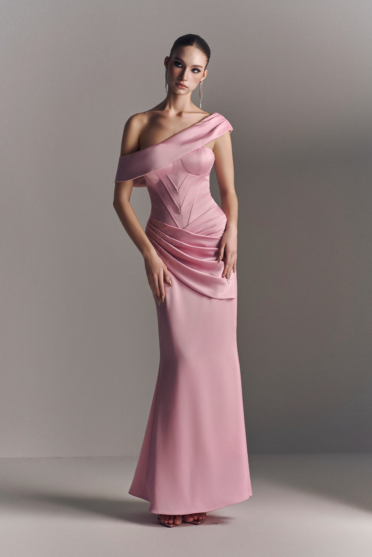 Woman wearing a pink one-shoulder evening gown against a plain background