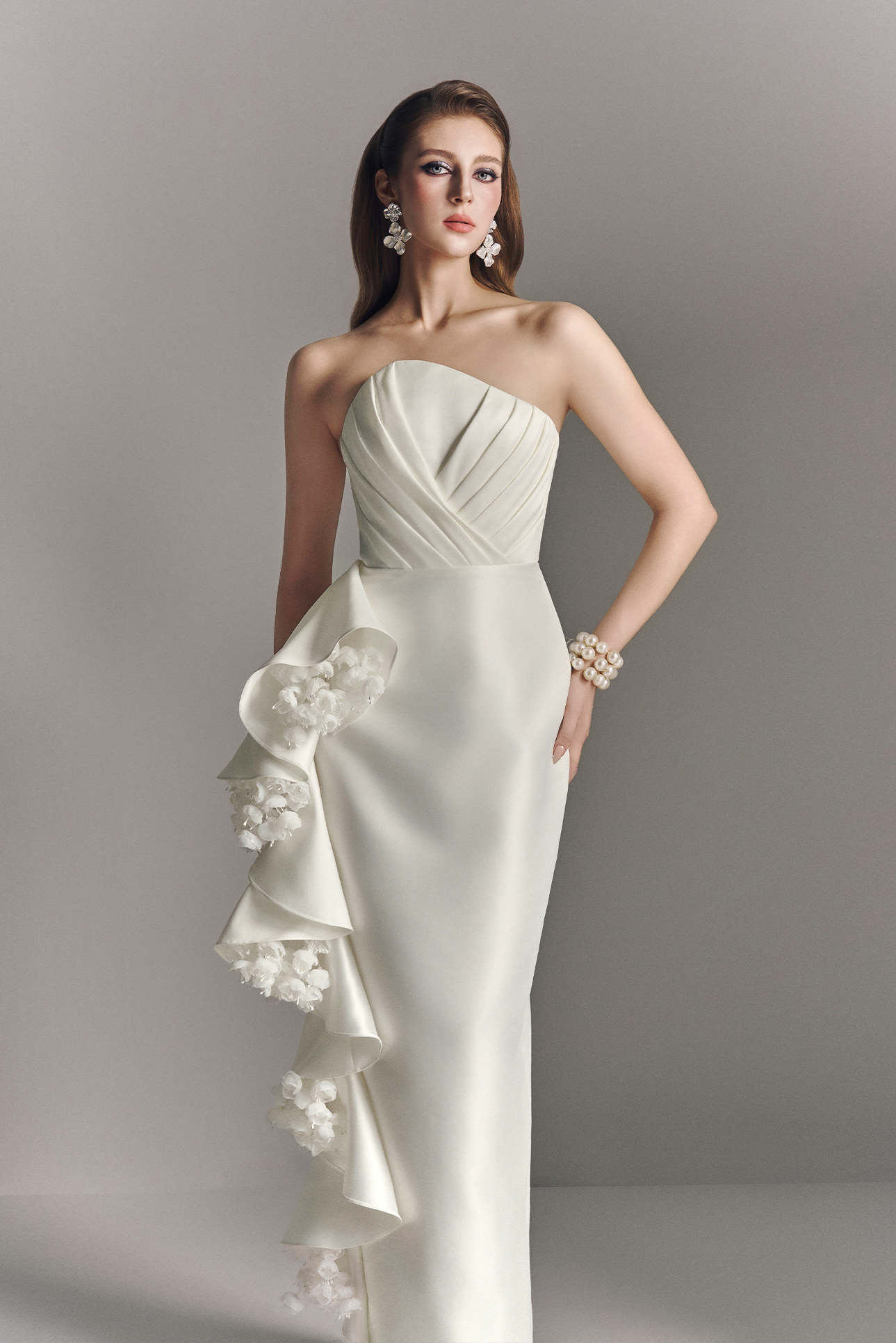 Woman wearing a white strapless gown with floral details on a gray background