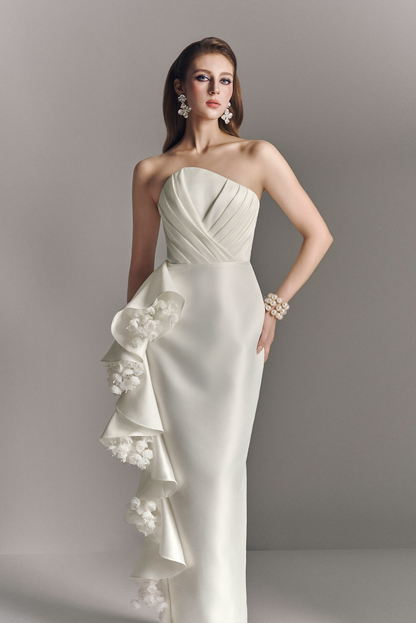 Woman wearing a white strapless gown with floral details on a gray background