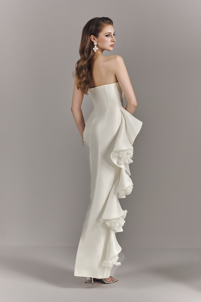 Woman wearing a strapless white gown with ruffled layers on a gray background