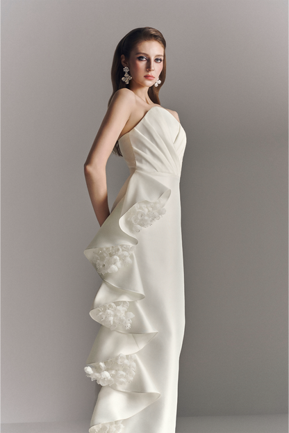 Woman wearing a white one-shoulder wedding dress with lace details against a plain background