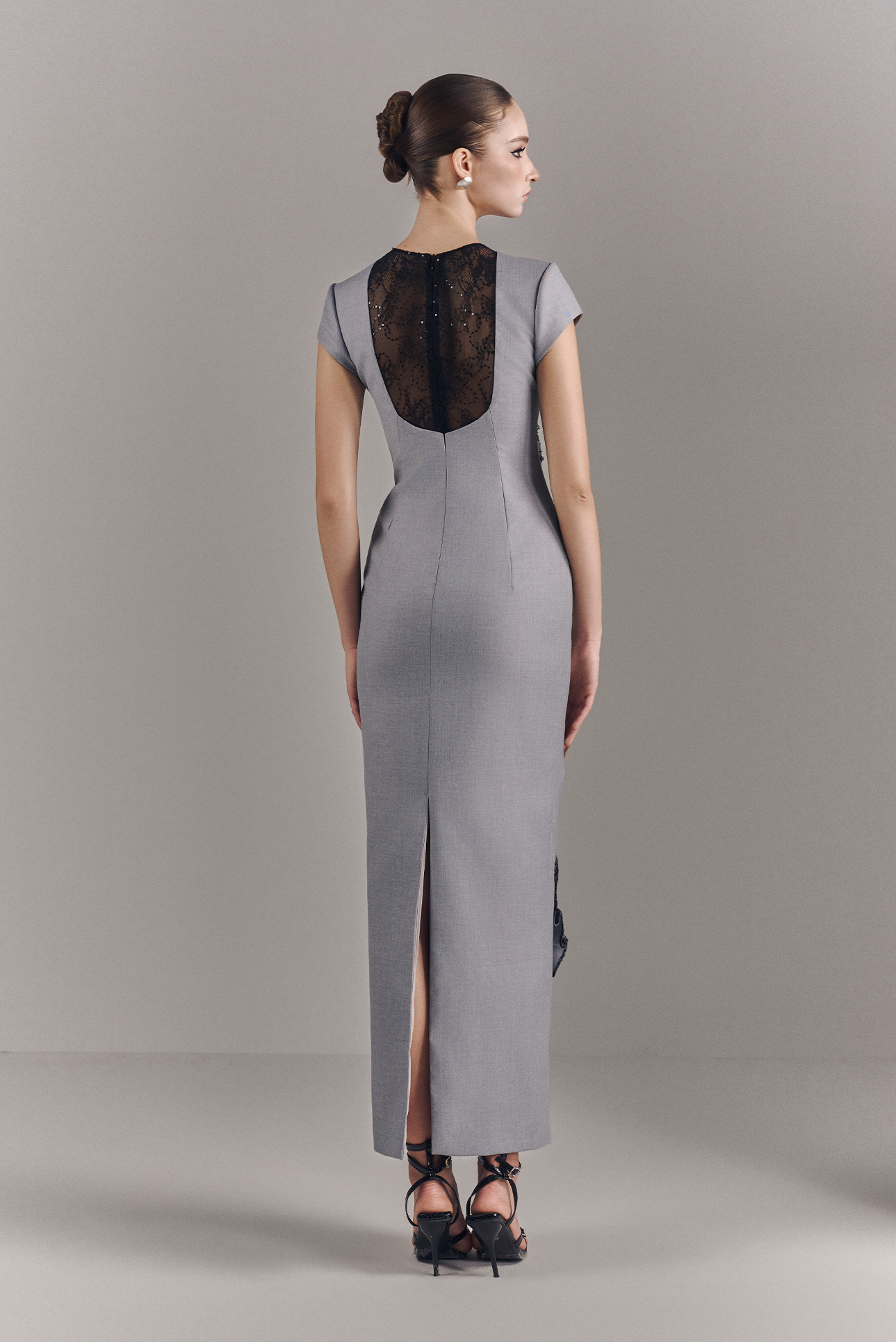 Woman wearing a gray dress with a black lace back on a plain background