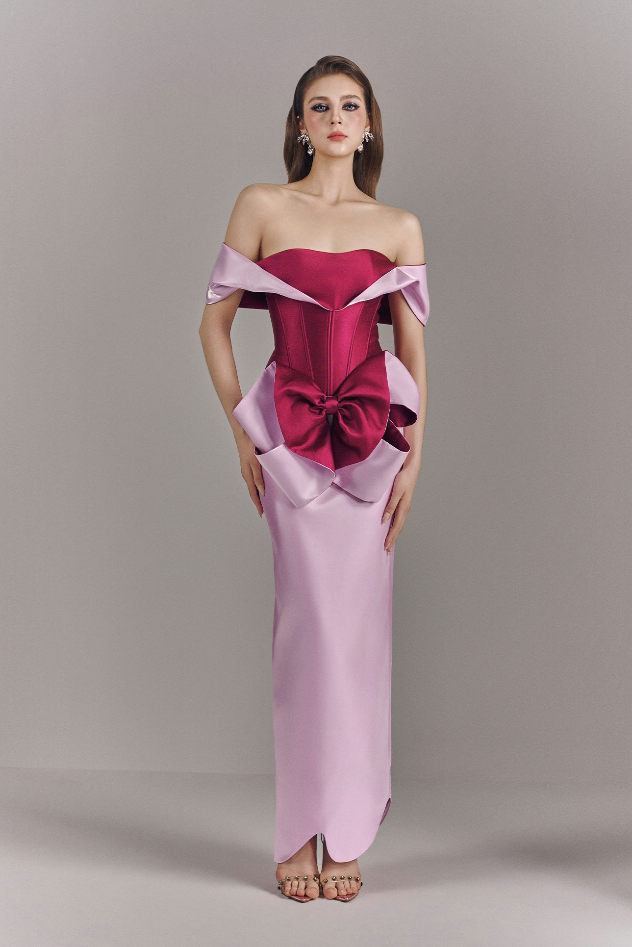 Woman wearing a pink and red off-shoulder evening gown against a gray background