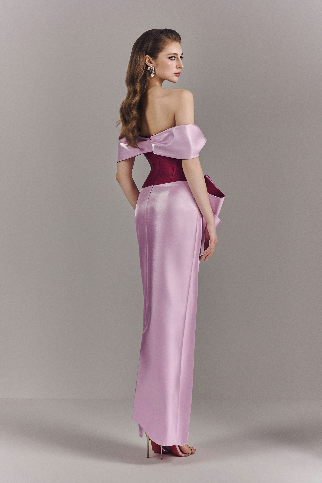 Woman wearing a two-tone off-shoulder evening gown on a plain background