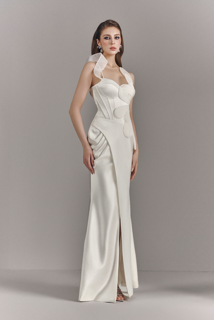 Woman wearing a white evening gown with a high slit on a plain background