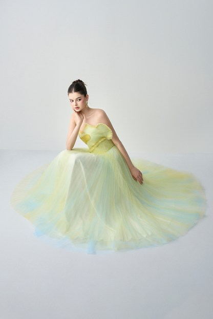 Woman wearing a yellow strapless gown with a flowing skirt on a light gray background