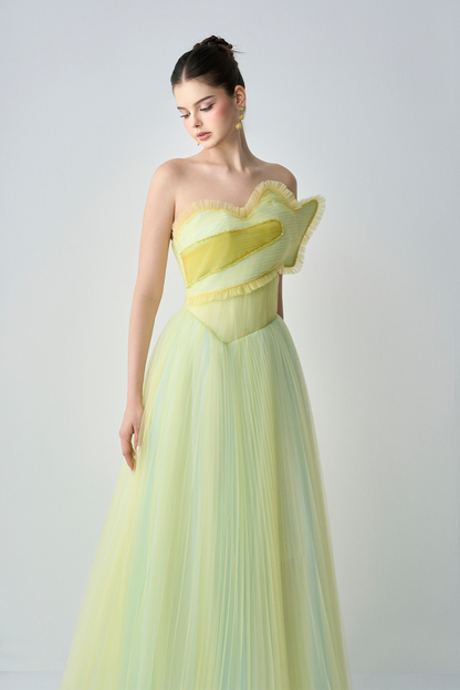 Woman wearing a strapless yellow evening gown against a plain background