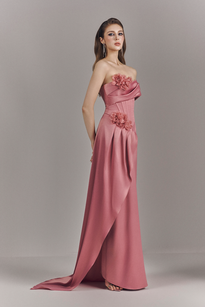 Woman wearing a strapless pink gown with floral details on a plain background
