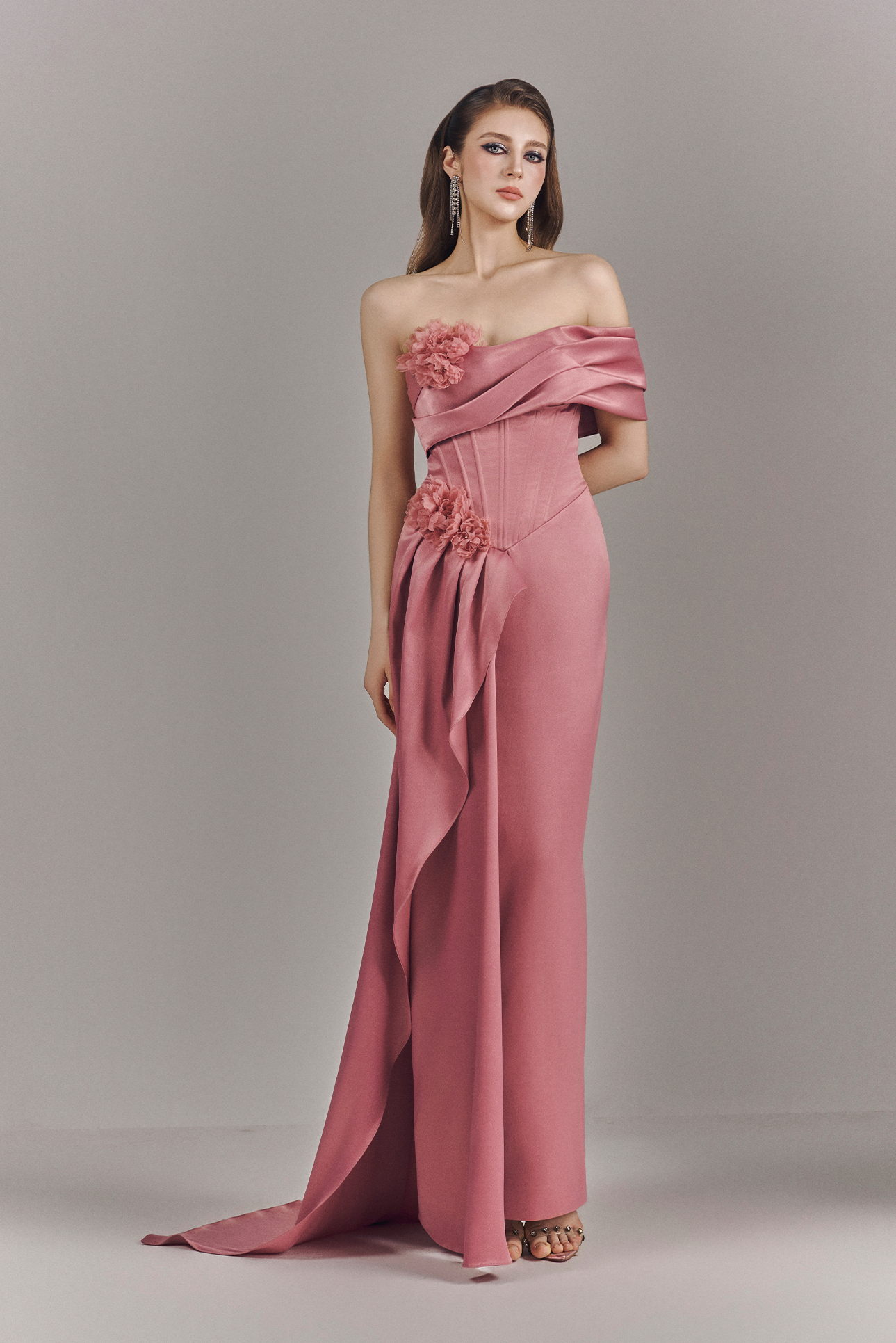 Woman wearing a pink strapless gown with floral details on a gray background