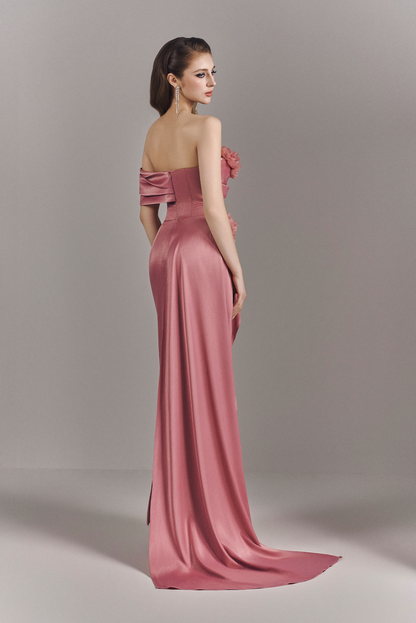 Woman wearing a pink evening gown with a floral detail on a plain background