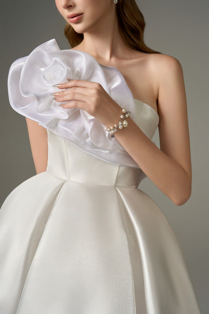 A close-up view of the bodice and shoulder of a graceful white flared micro-mini dress, emphasizing the handcrafted floral embellishments on the one-shoulder strap and the texture of the fabric.