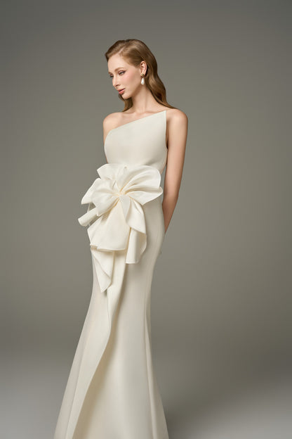 A close-up front view of a Devotion ivory acetate maxi dress, highlighting the asymmetric bandeau neckline and the elaborate 3D oversized handcrafted floral embellishment on the shoulder.