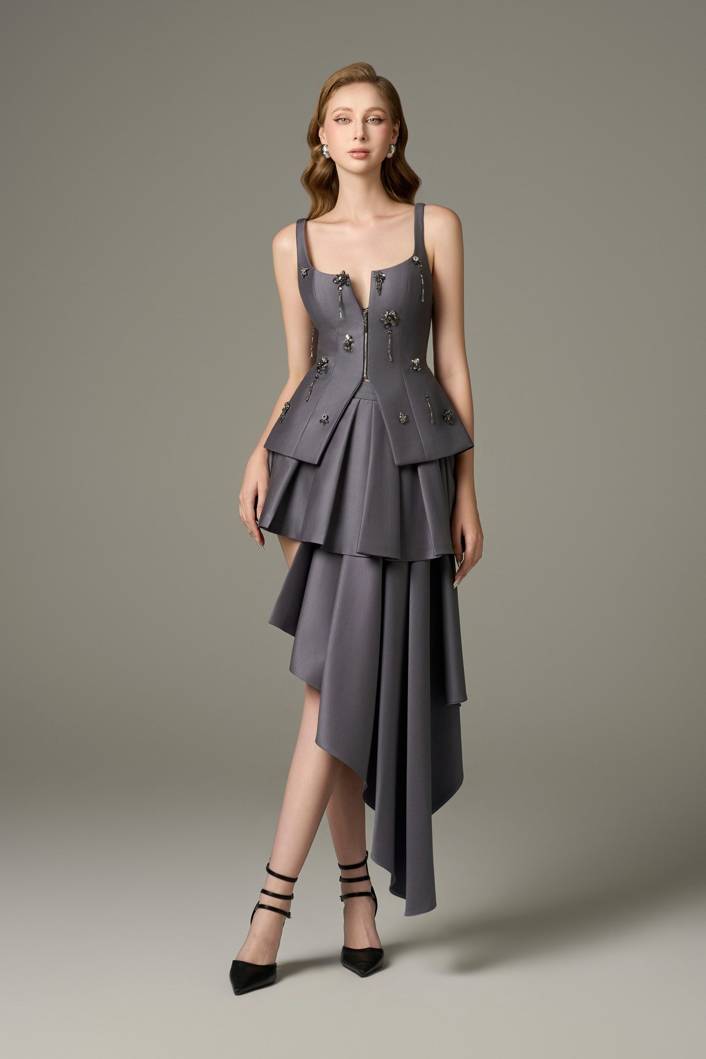  A full-length front view of a Lure grey stone embellished corset top and asymmetrical mini dress set, featuring a deep V-neck, sleeveless design, and a multi-layered, asymmetrical hem with handcrafted stone and bead embellishments on the corset.