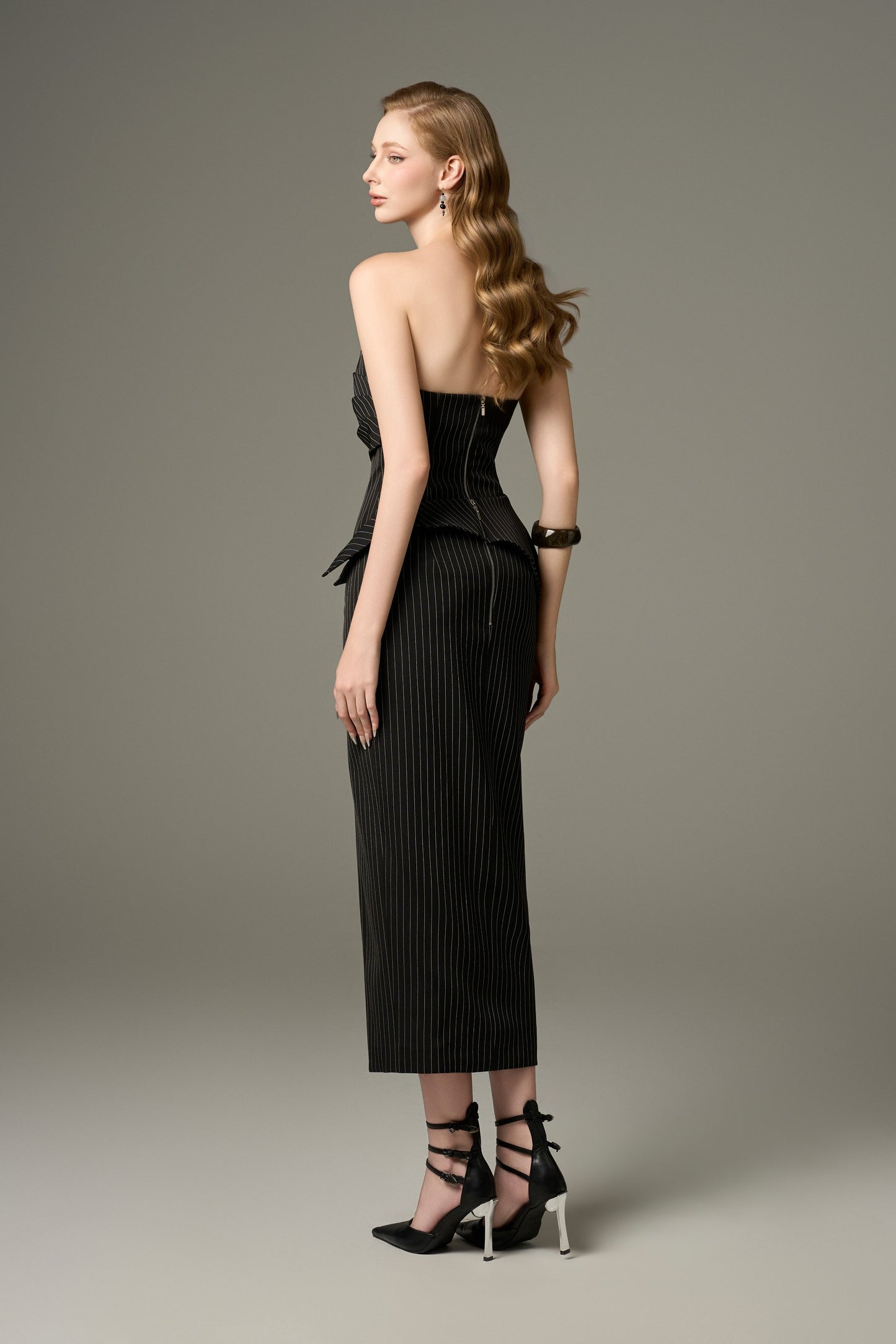 A back view of a Noir black stripe tweed set, showcasing the figure-hugging fit of the bandeau top and the long skirt.