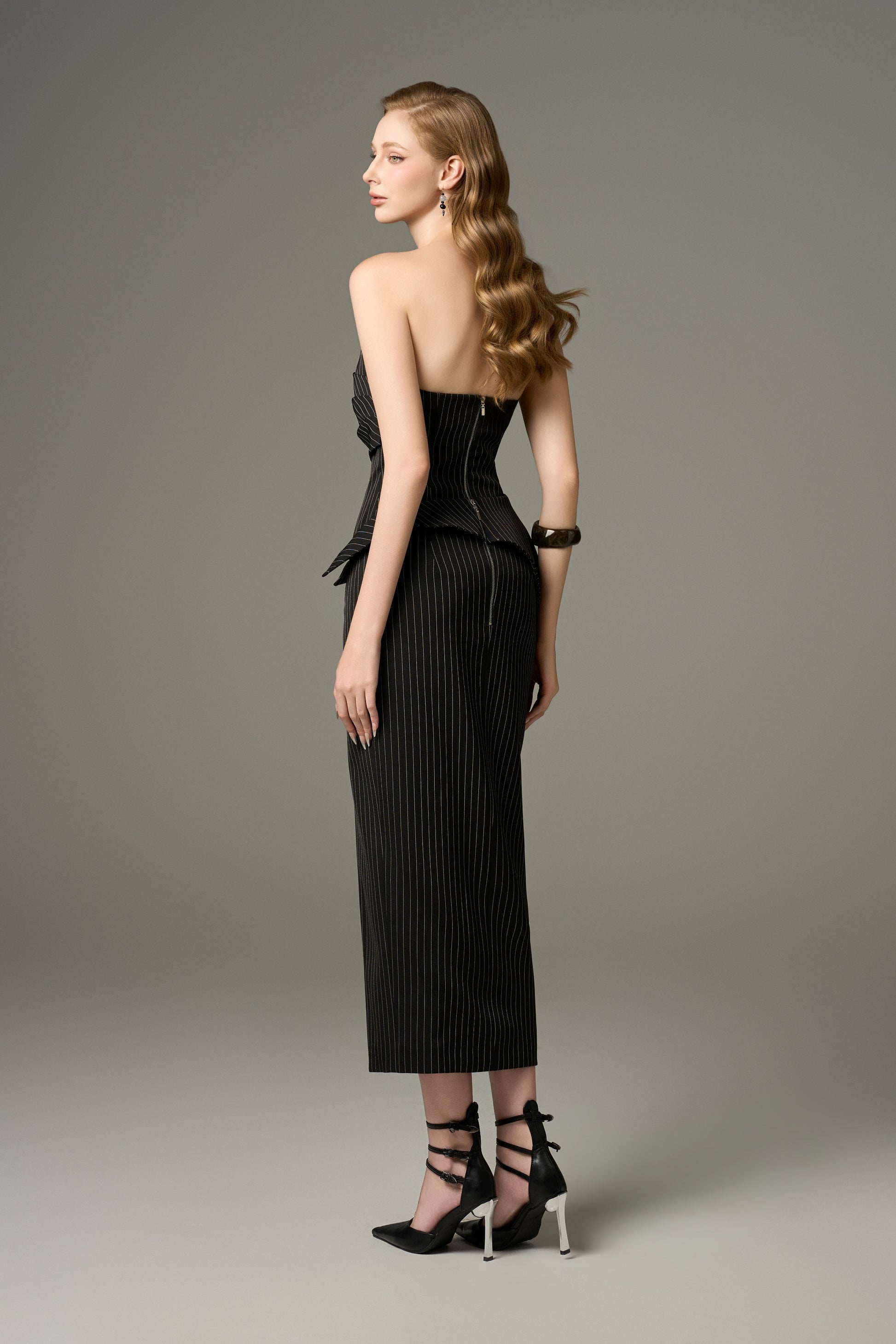 A back view of a Noir black stripe tweed set, showcasing the figure-hugging fit of the bandeau top and the long skirt.