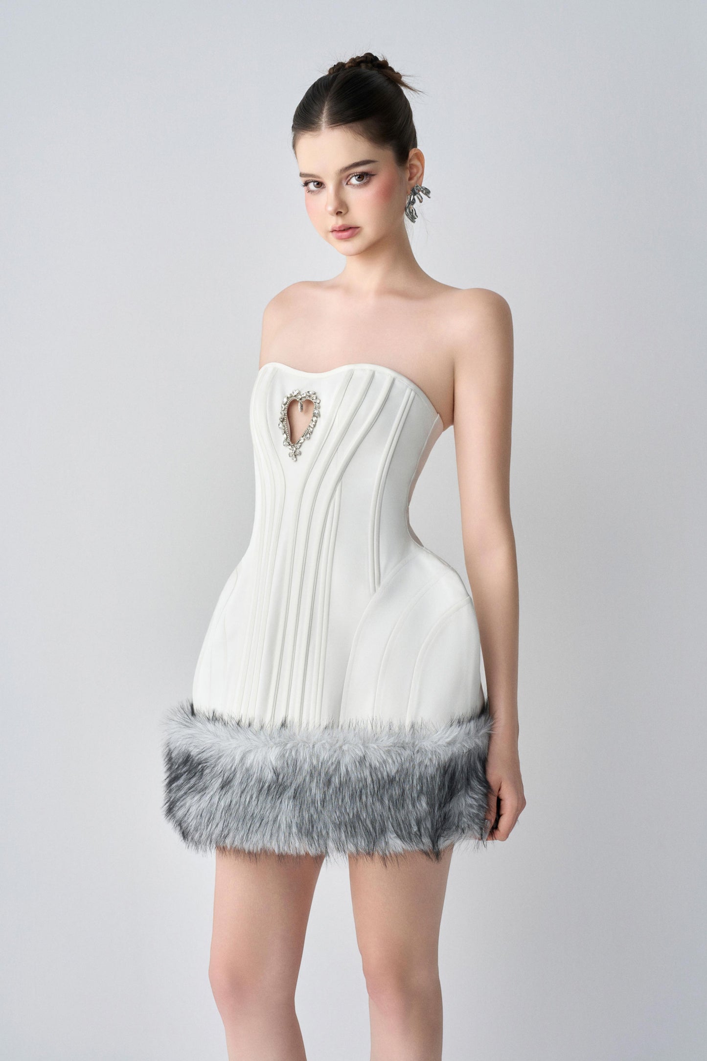 Woman wearing a white strapless dress with feather details on a gray background