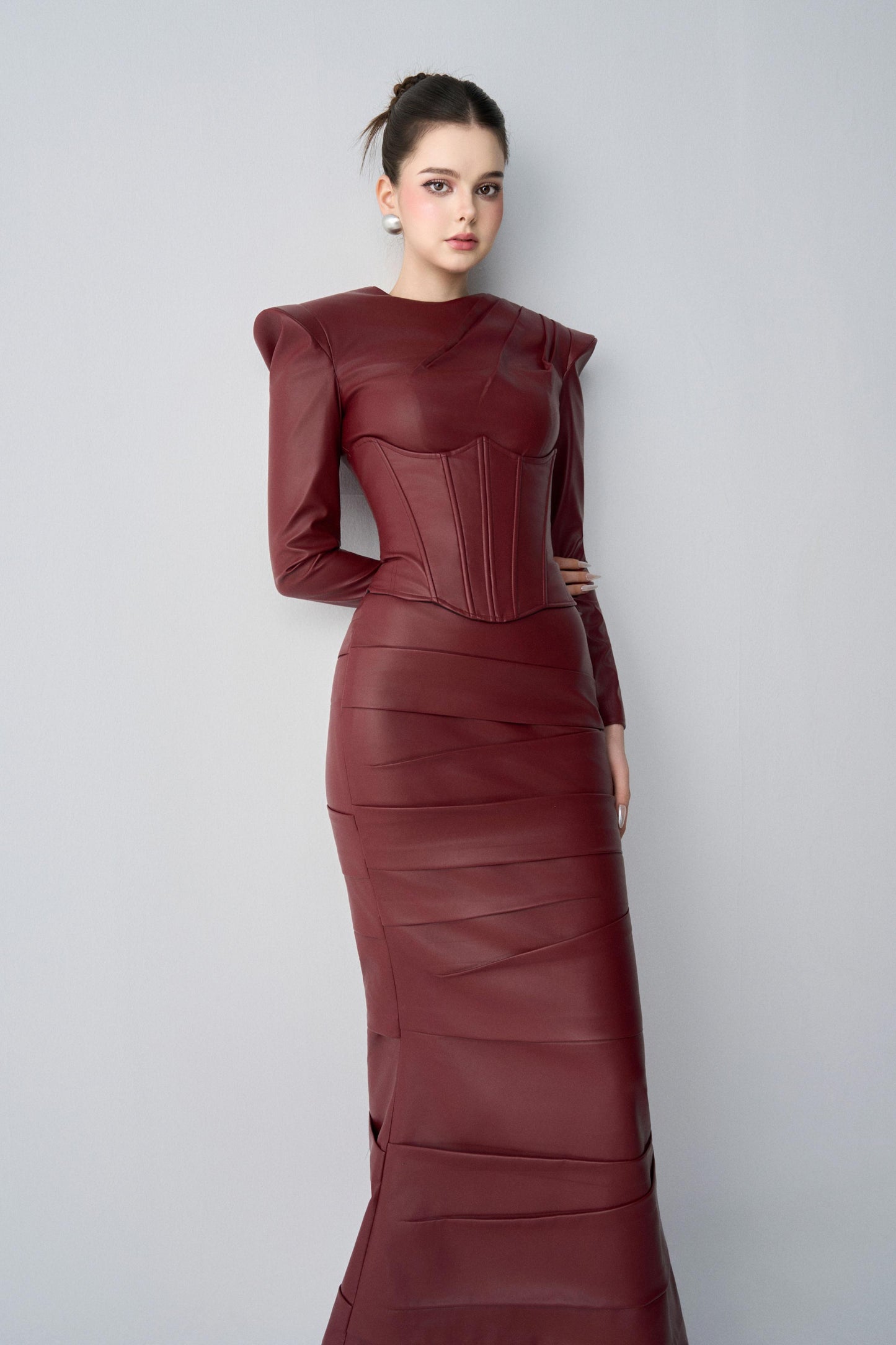 Model wearing a burgundy leather dress against a light gray background