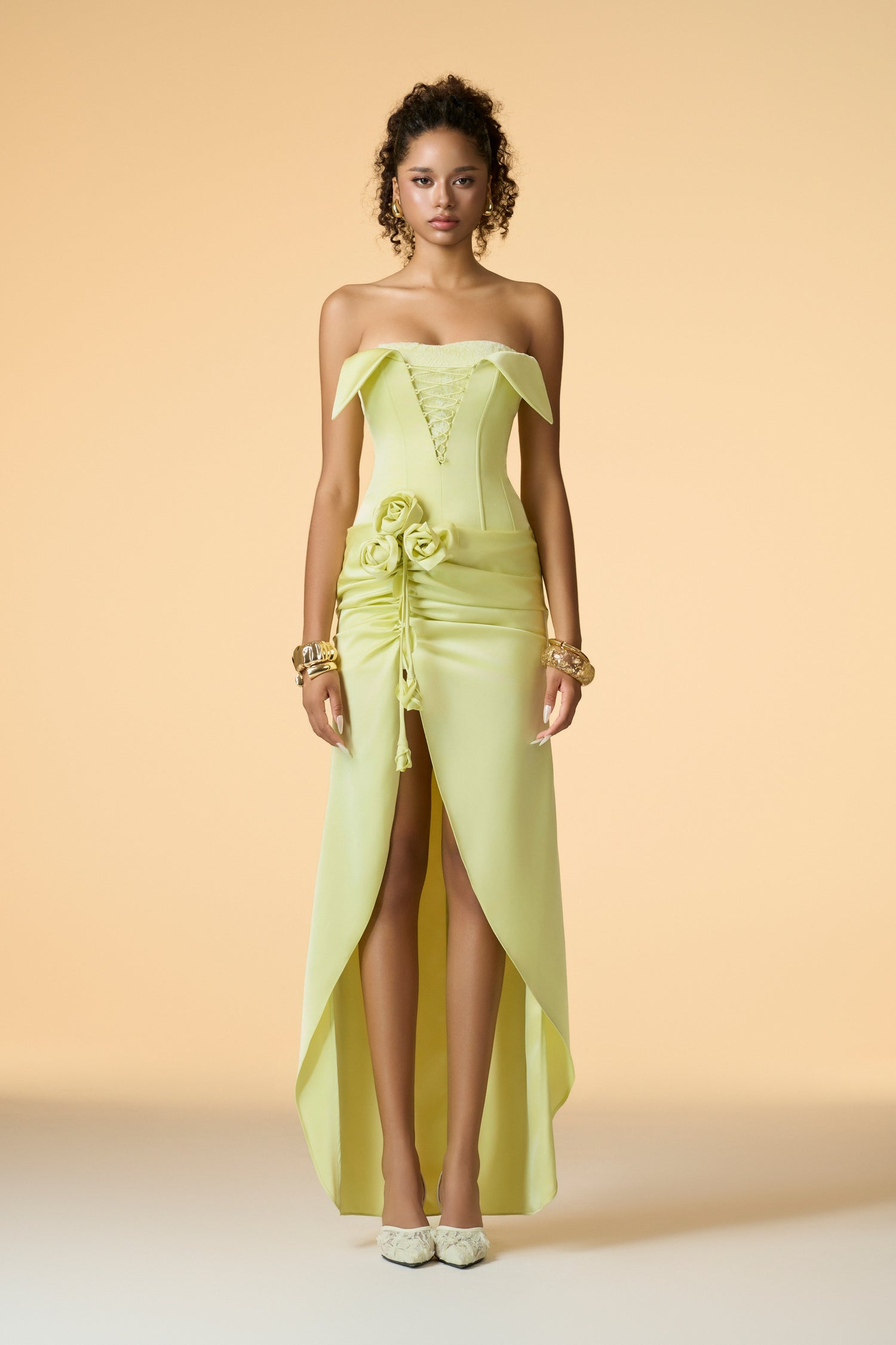  A vibrant neon pink sleeveless maxi dress, highlighting its folded neckline, lace-up front corset bodice, and a handcrafted rose embellishment on the side. The dress features a high-low skirt with a front slit.