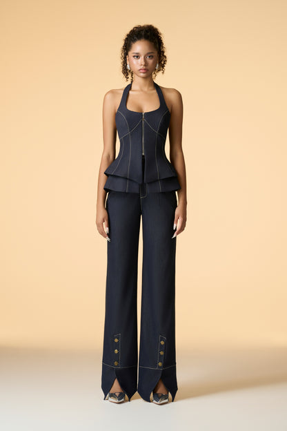 A close-up of a light blue two-piece set, emphasizing the details of the sleeveless halter-neckline corset top with its peplum-style waist and the wide-leg trousers with front slits and button embellishments.