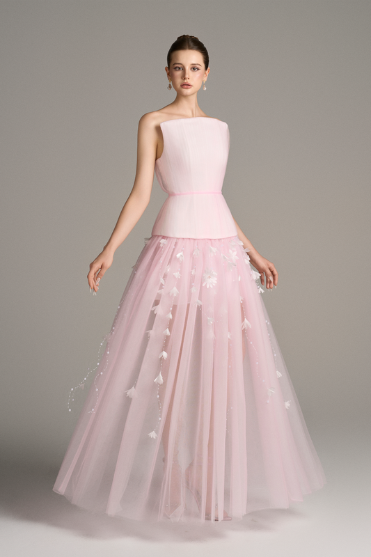 Front angled view of Aveta pastel pink two-piece maxi dress set with square neckline, corset bodice, and layered sheer skirt decorated with pearl and floral appliqué strands