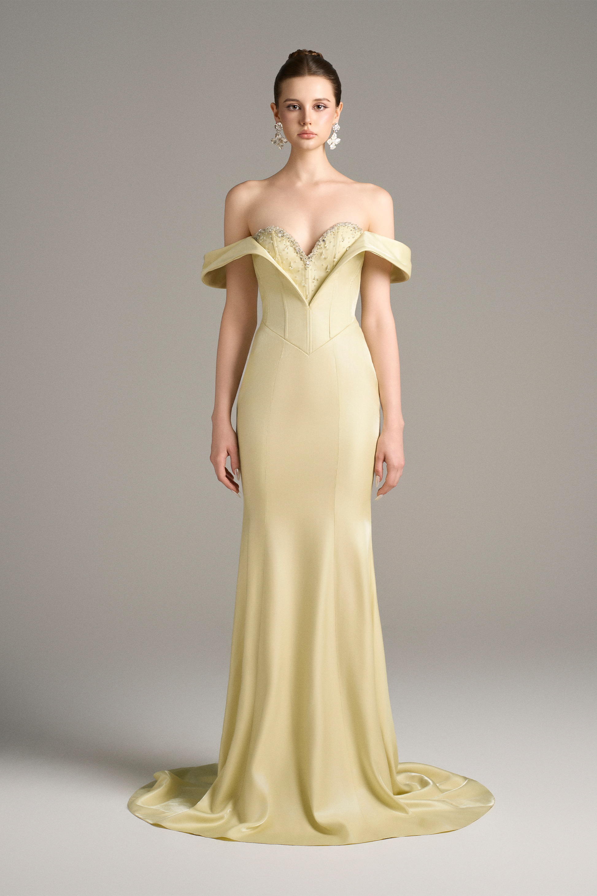 A model wearing an off-shoulder, lemon yellow silk mermaid gown with a sweetheart neckline, corset bodice, and crystal embellishments.