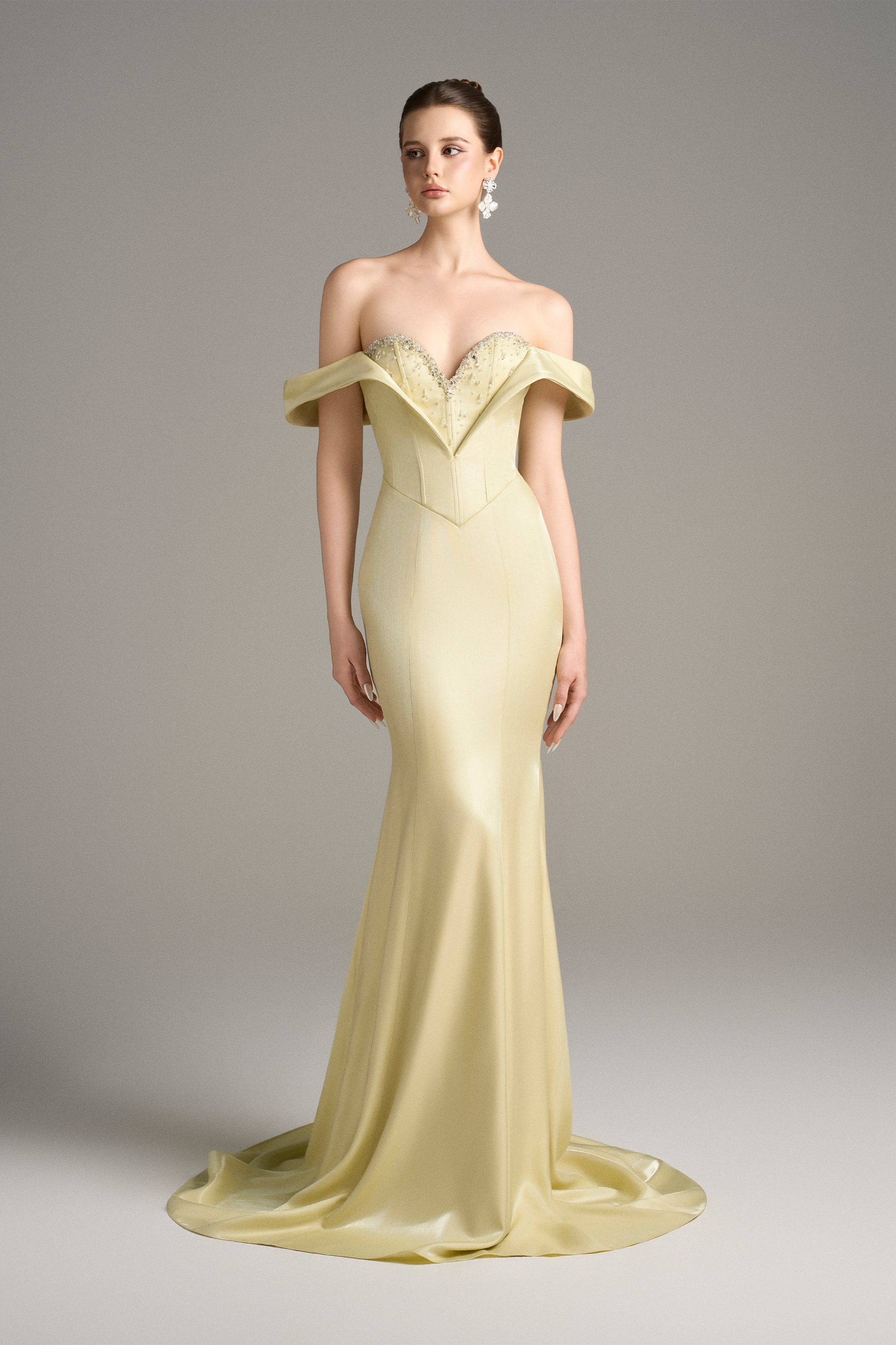 Full-length shot of a model in a lemon yellow off-shoulder mermaid gown with a corset bodice, sweetheart neckline, and beaded embellishments.