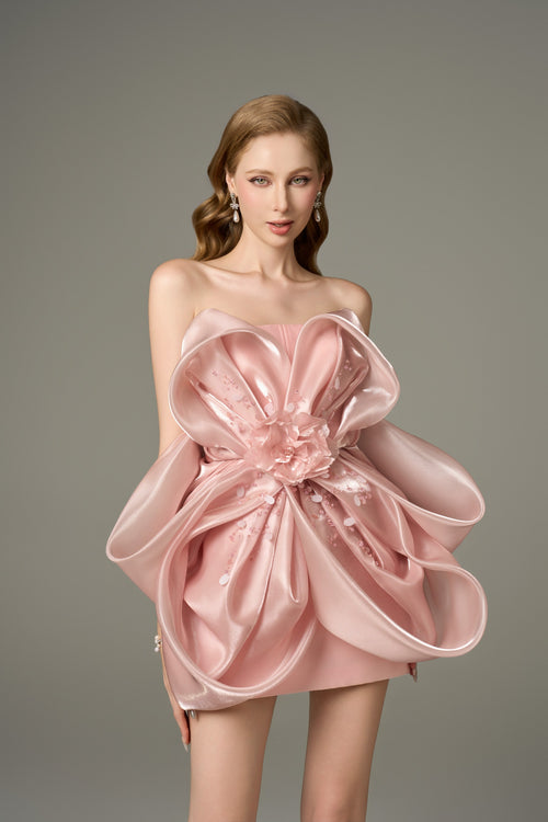 A close-up front view of a pink, sleeveless mini dress with a bandeau neckline, emphasizing the large, handcrafted 