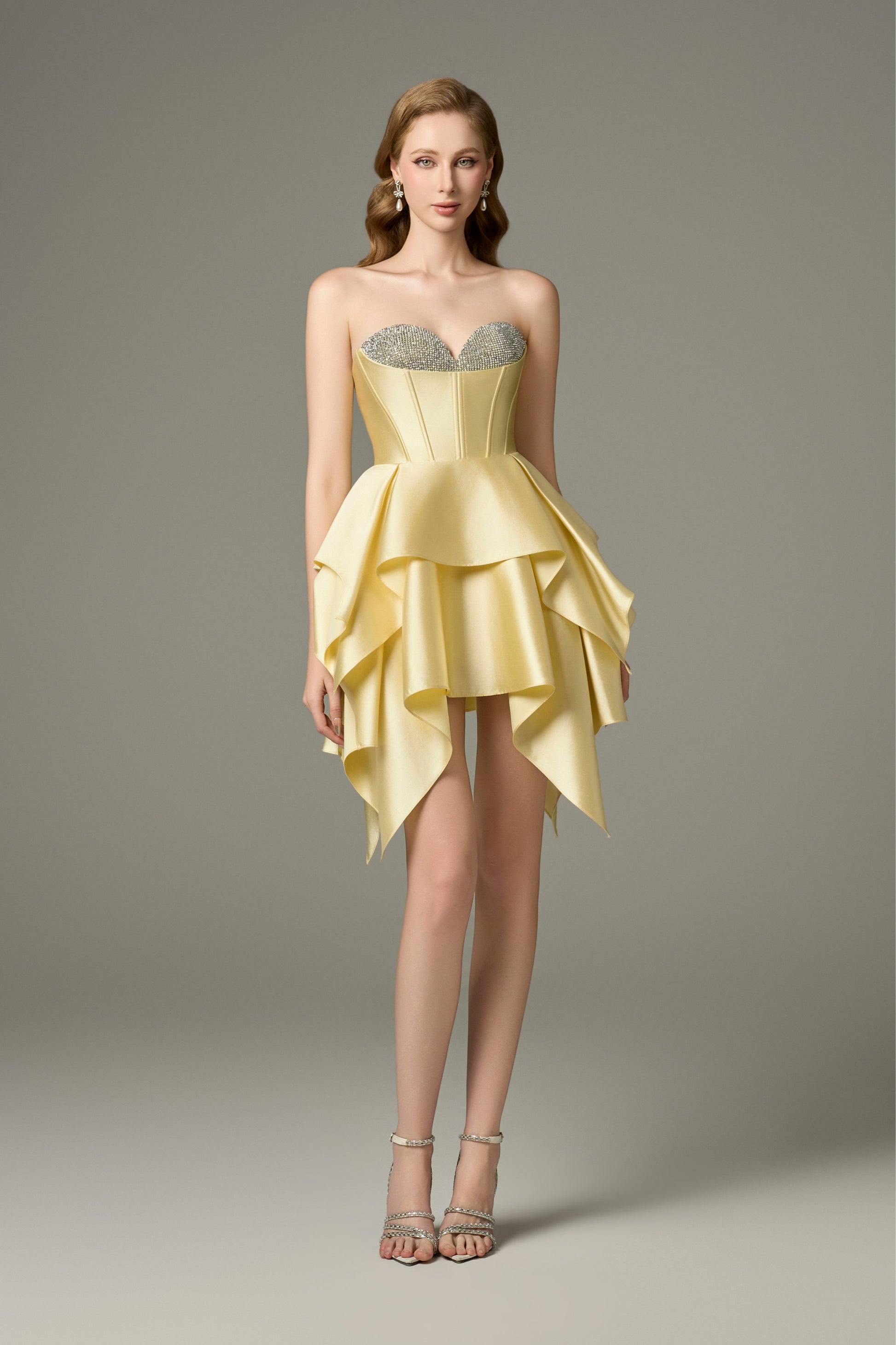 A full-length front view of a Soleil yellow bodycon mini dress featuring a sweetheart neckline with handcrafted crystal embellishments on the bust cups, a corset bodice, and a multi-layered, asymmetrical hem.